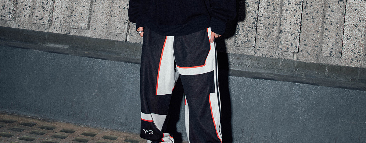 Sneaker archivist and connoisseur Kish Kash on a street in London's Soho wearing a black Y-3 adidas sweatshirt with white graphics, white and black Y-3 technical jogging bottoms with red edging and a black Y-3 belt bag and bucket hat