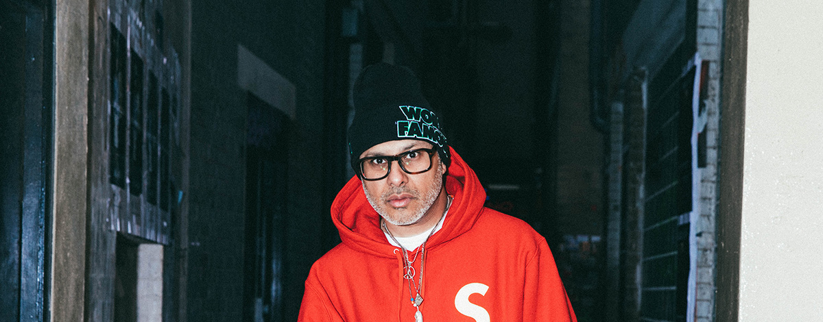 Sneaker archivist and connoisseur Kish Kash on a street in London's Soho wearing a red Supreme hooded sweatshirt and a black Supreme beanie