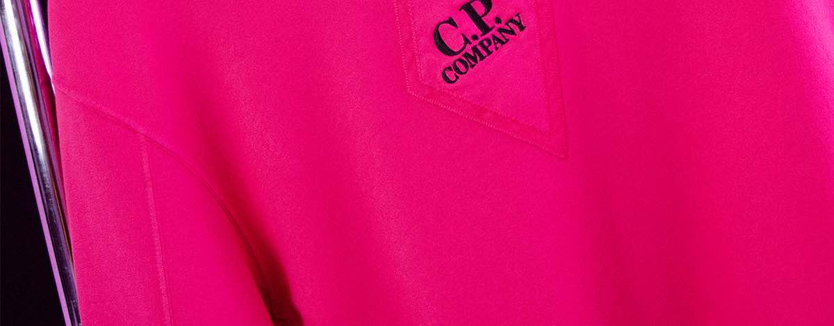 A close-up still life of the black C.P Company embroidered logo on the front of the FLANNELS X C.P. Company exclusive pink sweatshirt