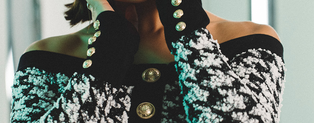 A close-up of Singer Raye wearing a matching Balmain black and white houndstooth off-the-shoulder top and skirt two-piece with gold Balmain buttons on the cuffs and down the front