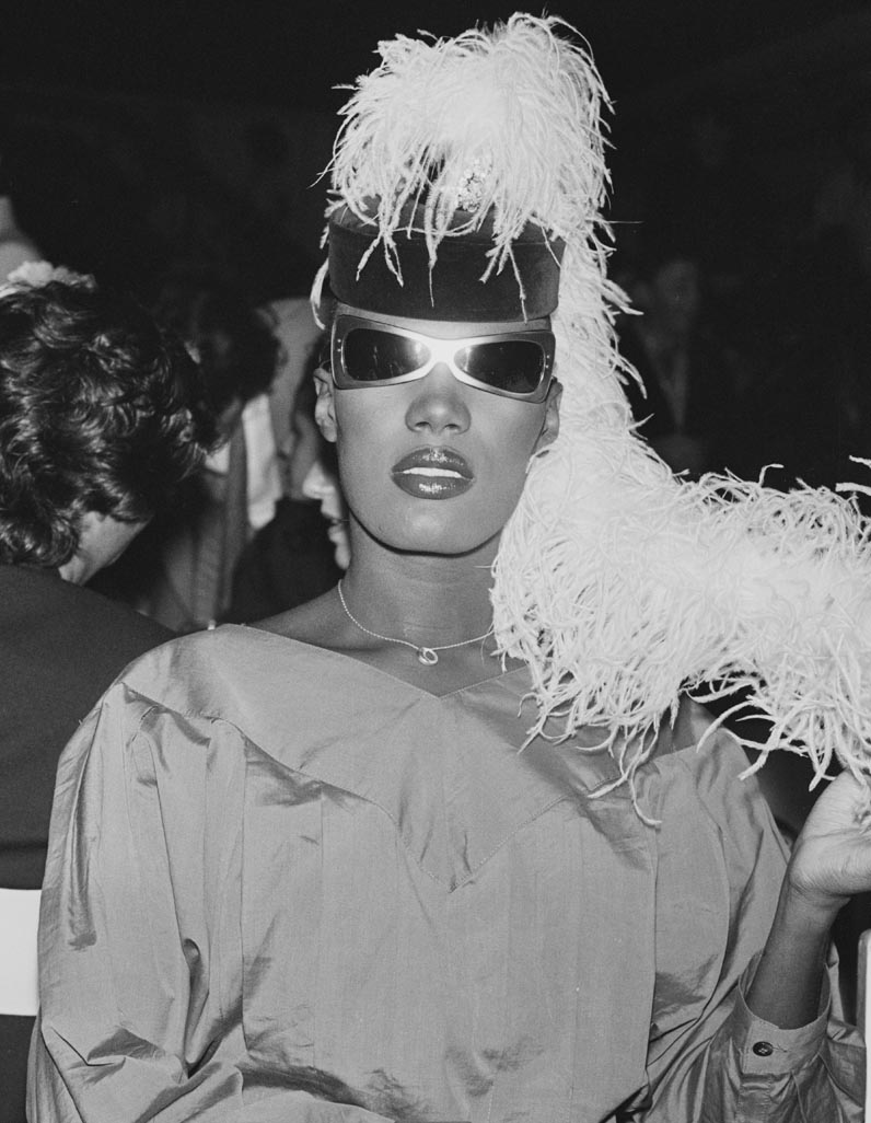 Grace Jones in sunglasses and hat and feathers