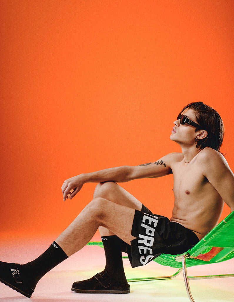 Male model sat on sun lounger in black swim shorts