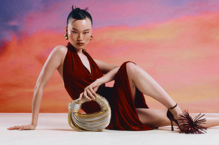 Female model half lying down in burgundy Bottega Veneta dress