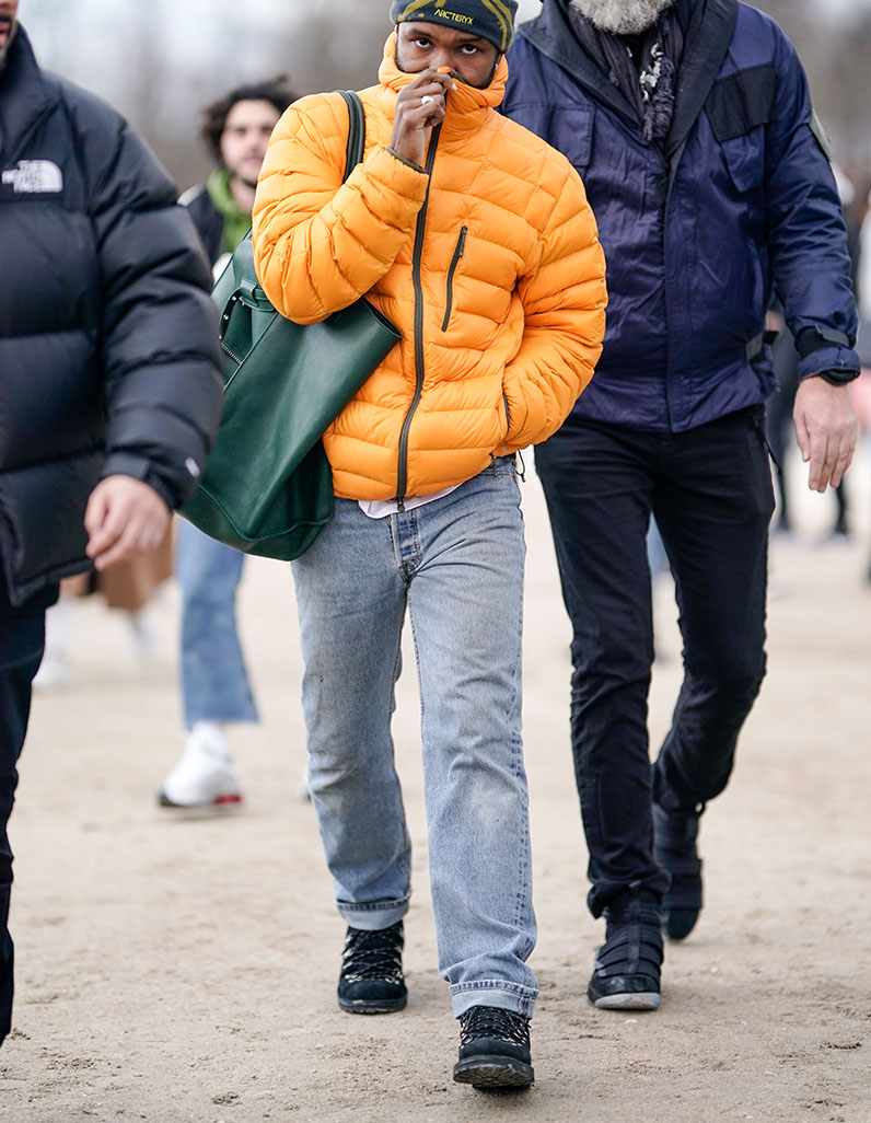 Frank Ocean in grey jeans, orange puffer jacket and black Salomons.